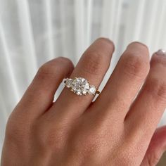 a woman's hand with three stone ring on top of her finger, in front of a white curtain