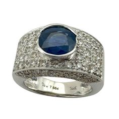 Indulge in luxury with our 18k Diamond and Sapphire Wide Band Ring. Featuring 1.40 carats of sparkling diamonds and a stunning 1.80 carat sapphire center, this sleek and modern ring is crafted in 18k white gold. With a weight of 5.6 grams and a size 6.50, it's the perfect statement piece for a sophisticated and exclusive look.   Condition: In good condition with some minor surface wear consistent with age. Ring size: 6.50 Markings: "750" "T864" "18k" Metal: 18k White Gold Weight: 5.6 grams Diamonds: 1.40 carats  Sapphire: 1.80 carats Wide Band Diamond And Sapphire Rings, Oval Sapphire Ring With Pave Setting In Platinum, Sapphire Diamond Ring With Pave Setting In White Gold, White Gold Sapphire Diamond Ring With Pave Setting, Platinum Sapphire Ring With Pave Setting In White Gold, Modern Sapphire Rings Gia Certified, Modern Sapphire Rings With Brilliant Cut, Luxury Sapphire Diamond Ring In 14k White Gold, Luxury Round Cut Sapphire Ring With Pave Setting