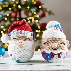 two crocheted santas sitting next to each other on a table near a christmas tree