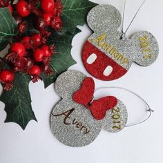 two mickey mouse christmas ornament hanging from a holly tree with red and silver decorations