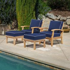 two wooden lounge chairs sitting next to a pool with blue cushions on it's sides