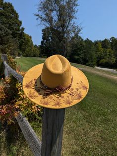 This tumeric yellow hand burnt wide brim fedora would make a perfect addition to any nature lover's wardrobe. The faux suede earthen yellow material burns a rich brown allowing the design to stand out. On the backside brim of the hat I hand burnt and shaded dandelion plants. On the front of the crown I burnt a single dandelion plant. I distressed the hat with stitch marks along the crown and brim of the hat. The design is original and completely free-handed. For a finishing touch I added a brown Handmade Yellow Wide Brim Straw Hat, Bohemian Yellow Straw Hat With Short Brim, Yellow Bohemian Straw Hat With Short Brim, Yellow Bohemian Wide Brim Straw Hat, Yellow Fedora Sun Hat For Kentucky Derby, Adjustable Brimmed Yellow Fedora, Adjustable Yellow Brimmed Fedora, Yellow Curved Brim Fedora For Kentucky Derby, Yellow Fedora Hat For Fall