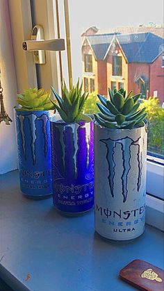 three cans with plants in them sitting on a window sill