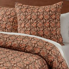 a bed with brown and orange bedspread on top of it next to a night stand