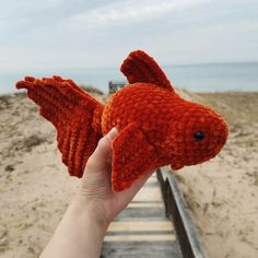 a hand is holding an orange crocheted fish on the boardwalk at the beach