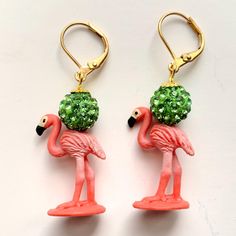 two pink flamingos with green balls on their heads are hanging from gold - plated hooks