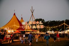 many people are walking around at an outdoor fair with tents and lights in the background