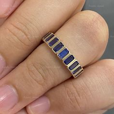 a woman's hand holding a gold ring with blue sapphire stones on it,