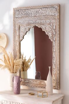 a mirror sitting on top of a white mantle next to a vase filled with flowers