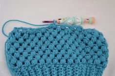 a crocheted blue bag with a toy on top of it