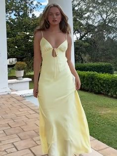 a woman in a yellow dress is standing on a brick walkway and posing for the camera