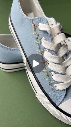 a pair of blue tennis shoes with embroidered flowers on the side and white laces