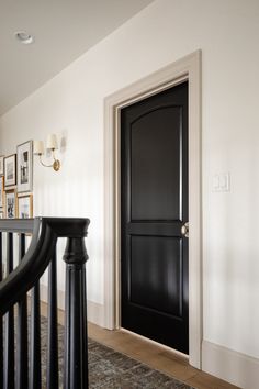 a black door in a white room next to a stair case with pictures on the wall