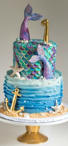 a three tiered cake decorated with blue and purple icing, topped with a mermaid tail