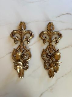 two ornate gold wall sconces on a marble counter top, one with an acantic design