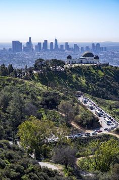 the city skyline is seen in the distance as cars drive along a road on a hill