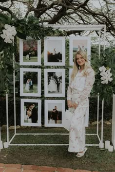 a woman standing in front of a white photo frame with photos on it and flowers