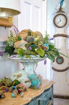 a vase with flowers and seashells on a table in front of a clock