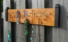 a wooden sign with many different necklaces hanging on it's side next to a fence