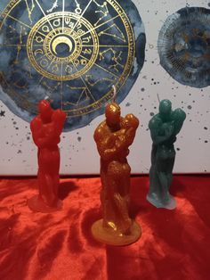 three small figurines sitting on top of a red cloth covered table next to a clock