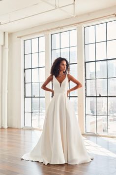 a woman in a white wedding dress standing on a wooden floor next to large windows