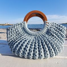 a knitted bag sitting on top of a sandy beach next to the ocean with a wooden handle