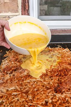 a person pouring sauce into a bowl on top of wood shavings in front of a window