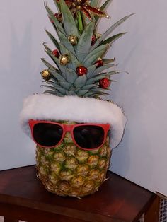 a pineapple wearing sunglasses and a santa hat is sitting on a small wooden table