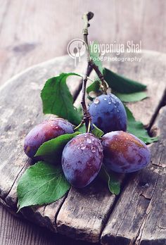 three plums on a wooden board with green leaves