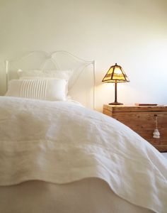 a bed with white linens and a lamp next to it on a nightstand in a bedroom