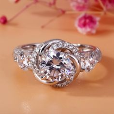 an engagement ring with three stone center surrounded by two smaller round diamonds on a table next to pink flowers