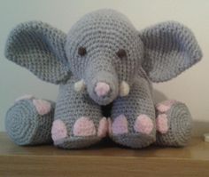 a crocheted stuffed elephant sitting on top of a wooden table next to a white wall