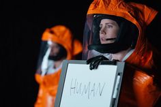 two people in orange spacesuits holding a sign