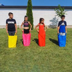 four children standing in the grass with colorful bags