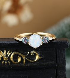 a white opal and blue topazte ring sitting on a black box next to a flower