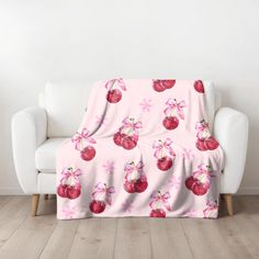 a pink blanket with cherries on it sitting in front of a white couch and chair