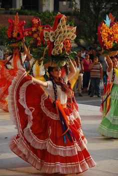 several women in colorful dresses are dancing on the street with their hands up and holding flowers