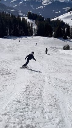 a man riding a snowboard down the side of a snow covered slope in front of mountains