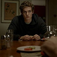 a young man sitting at a table with food in front of him and two other people