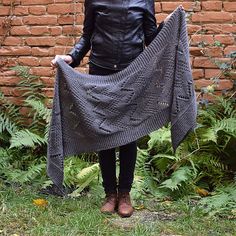 a woman holding up a gray knitted shawl