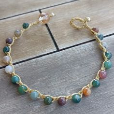 a gold chain bracelet with multi colored stones on it's end, sitting on a wooden surface