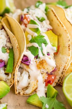 three fish tacos with limes, cilantro, and sour cream sauce