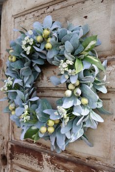 a wreath is hanging on the side of an old door with green leaves and white flowers