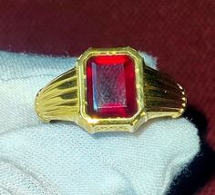 a gold ring with a red stone in it on top of a white cloth covered napkin