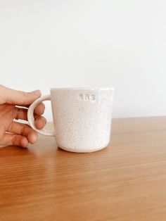 a hand holding a coffee cup on top of a wooden table