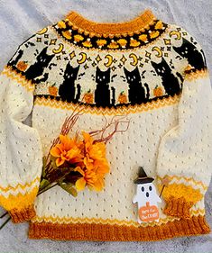 a white sweater with an orange flower and a small snowman on the front is sitting next to it