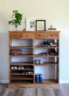 a wooden shelf with shoes on it next to a potted plant and framed pictures