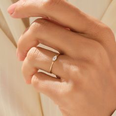 a woman's hand wearing a gold ring with a diamond on the middle finger