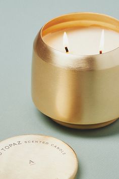 a gold candle sitting next to a round wooden coaster on a blue surface with the words do notz scented candles written in it