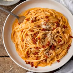 a white bowl filled with spaghetti and sauce on top of a wooden table next to a spoon